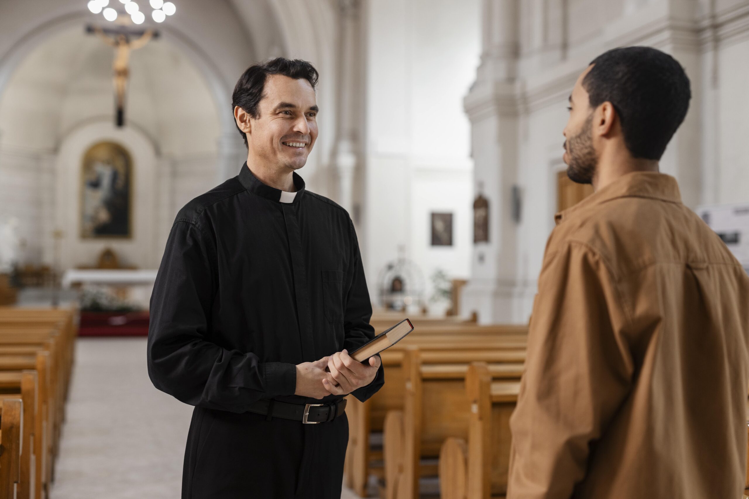 Priest holding a Bible and talking with a parishioner in church